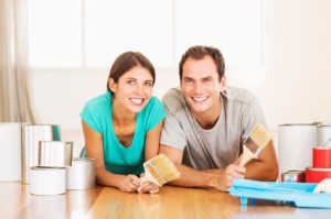 Happy Couple With Paint Brushes And Cans Looking Away